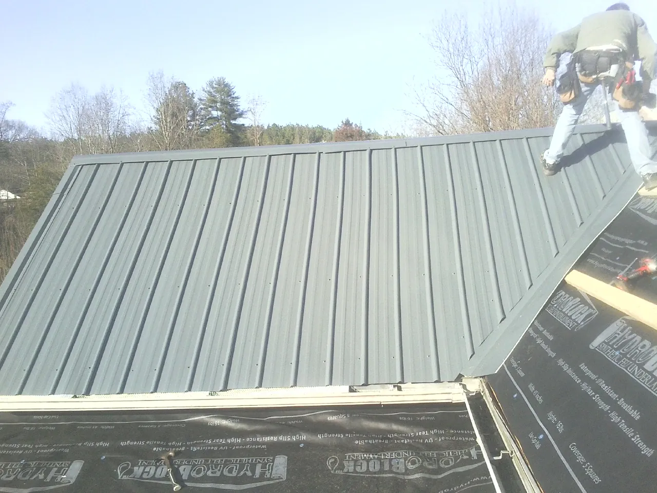 Crew installing dark green standing seam panels over synthetic underlayment in Linden